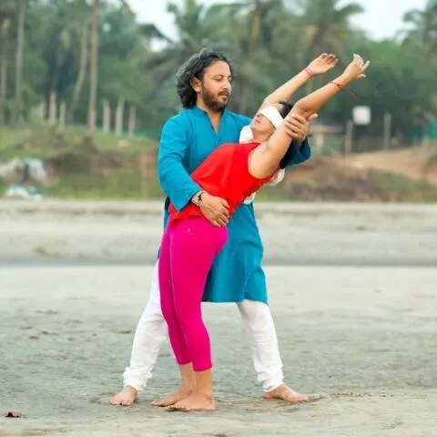 A yoga instructor assisting a blindfolded student in a standing on a beach