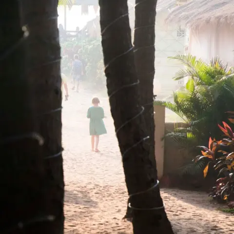A young girl walking down a sunlit sandy path