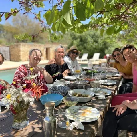 A group of people enjoying a meal together at a long wooden table outdoors