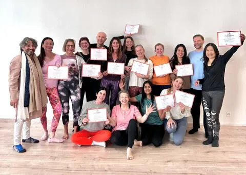 A group of smiling people posing together in a bright studio, holding up certificates.