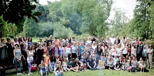 A large group of people of all ages posing together on a grassy field in front of a lush forest.