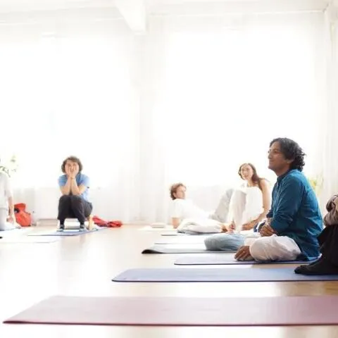 A bright, minimalist studio where several students are seated on yoga mats