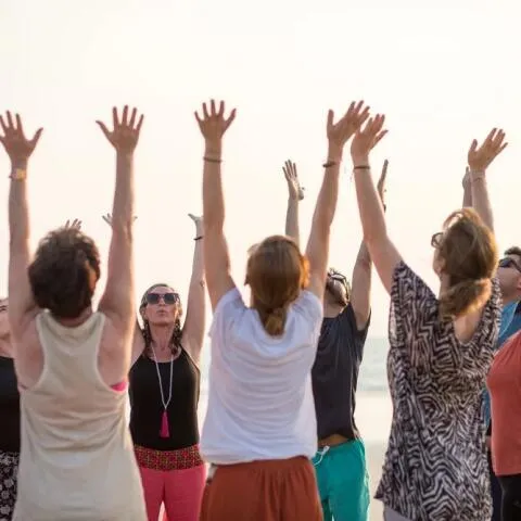 A group of people standing in a circle on a beach at sunset