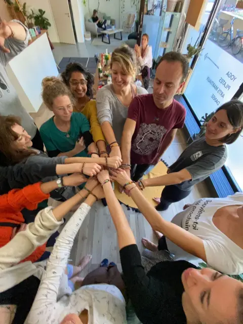 A diverse group of people standing in a circle join hands in the center, showing unity and friendship.