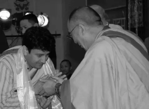 A black and white photo of Yogalife founder Sanjeev Bhanot bowing as he holds hands with His Holiness the 14th Dalai Lama during a meeting.