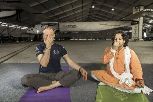 Yogalife founder Sanjeev Bhanot and another man practice alternate nostril breathing while sitting on yoga mats in front of the Solar Impulse aircraft.