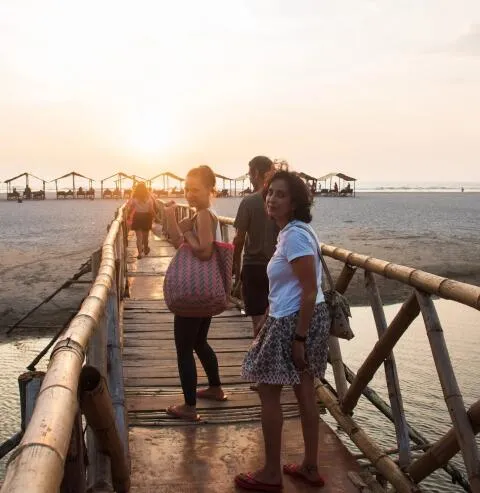 Two women smiling while walking across a bamboo bridge