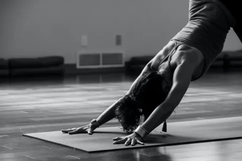 A black and white close-up of a person performing a downward-facing dog pose on a yoga mat in a studio.