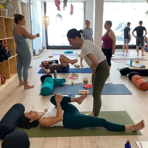 A yoga teacher providing a hands-on adjustment to a student lying on a mat
