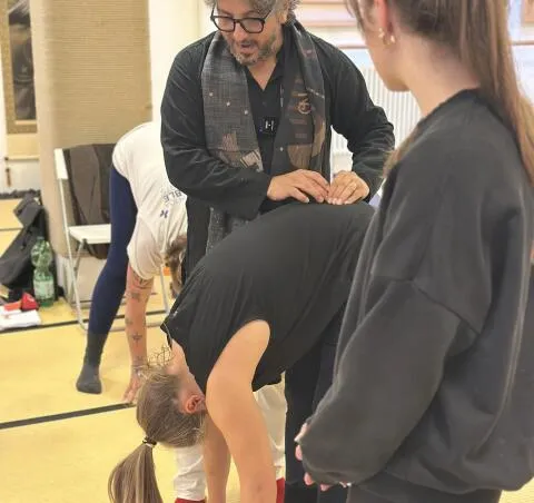 A yoga instructor providing a hands-on adjustment to a student