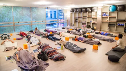A group of people lying on yoga mats under blankets in Savasana during a guided Yoga Nidra session in a studio.