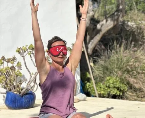 A woman sitting with her arms raised during an outdoor yoga session.