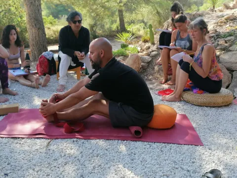 A group of people participating in an outdoor yoga and mindfulness workshop in a wooded area.