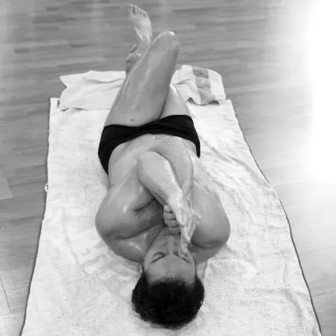 A person lying on a yoga mat with their arms and legs intertwined