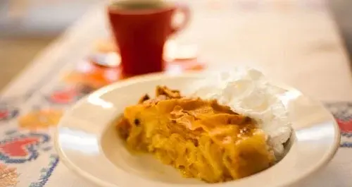 A slice of warm strudel with whipped cream next to a red coffee cup.