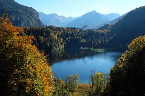 A serene lake surrounded by autumn trees and mountains in the Bavarian Alps.