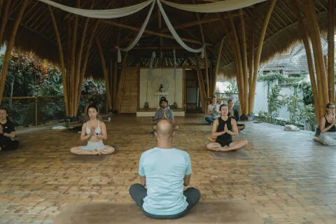 Instructor leading a group meditation session inside an open-air bamboo shala