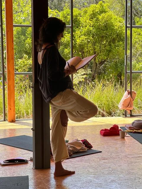 Woman standing in tree pose while writing in a notebook near a sunlit window